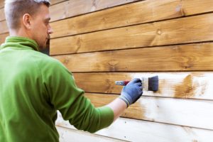 Hillsboro worker painting house exterior with brown wood protective color